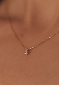 Gouden ketting met een kleine hanger voorzien van een doorzichtige edelsteen, gepresenteerd tegen een tekstuurrijke huidachtergrond.