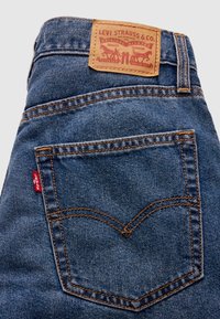 Poche arrière et ceinture d'un jean Levi's bleu avec coutures orange, étiquette rouge Levi's et patch en cuir avec le logo Levi Strauss.