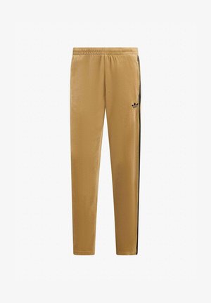 Pantaloni della tuta Adidas color cammello con strisce laterali nere e logo trefoil Adidas nero sulla coscia sinistra, dotati di cintura elastica.