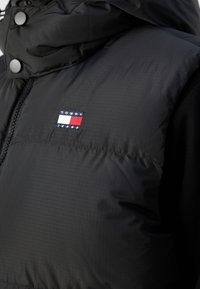 Veste matelassée noire avec zip et boutons-pression, avec un petit patch logo Tommy Jeans sur la poitrine.