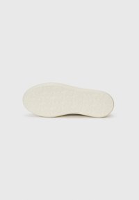 Light-colored rubber sole with a textured surface and small circular patterns. Features a logo embossed in the center for brand identification.