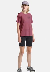 Chemise à manches courtes couleur marron clair avec un motif graphique, associée à un short noir et des chaussures de randonnée grises. Une casquette grise complète la tenue.