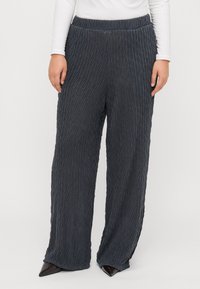 Pantalons larges gris foncé, présentant une texture froissée et une taille élastique. Accentués d'un éclat subtil, ourlés au niveau de la cheville.