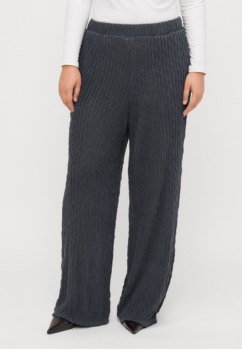Pantalons larges gris foncé, présentant une texture froissée et une taille élastique. Accentués d'un éclat subtil, ourlés au niveau de la cheville.