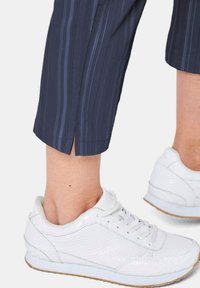 Marine gestreepte broeken met een lichte split aan de zoom, gecombineerd met witte gestructureerde sneakers met een lichte zool en veters.