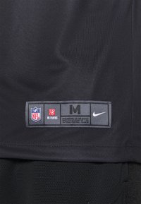 Etiqueta de una camiseta atlética negra de Nike que presenta los logos de la NFL y de los jugadores de la NFL, etiqueta de tamaño "M" y texto que detalla las especificaciones de la Liga Nacional de Fútbol Americano.