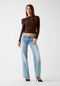 Haut marron à manches longues et épaules dénudées, associé à un jean droit bleu clair et des talons à imprimé animal ; tissu lisse et coupe ajustée.