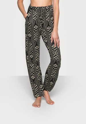 Black and cream patterned trousers with a loose fit, elastic waistband, and side pockets. Features geometric designs throughout.