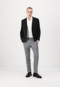 Schwarzer Blazer über einem weißen Hemd, graue Anzughose und schwarze Schuhe; glattes Material, taillierte Passform und minimalistisches Design.