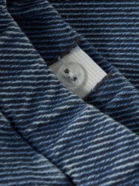 Denimtyg i mörkblått med ribbad struktur, med en vit tygetikett och en genomskinlig plastknapp i närbild.