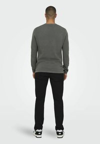 Grijze longsleeve shirt met een ronde hals, gecombineerd met zwarte broek en witte sneakers, gezien van achteren. Zorgt voor een gladde textuur en een aansluitend ontwerp.