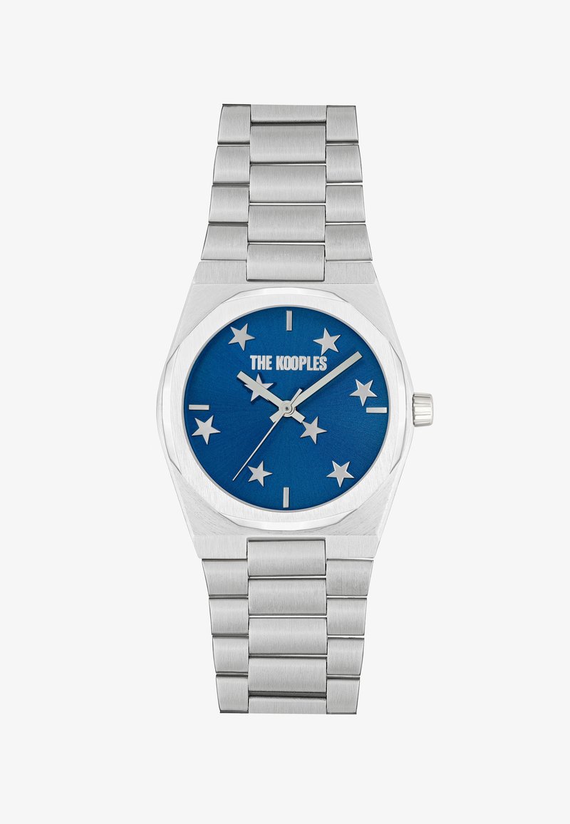 Sidabrinis metalinis laikrodis su mėlynu ciferblatu, kuriame yra žvaigždžių žymekliai, pažymėti "THE KOOPLES". Lygus nerūdijančio plieno apyrankės designas.