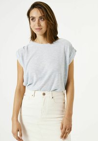 Top azul claro de manga corta con cuello redondo y puños enrollados, combinado con una falda de mezclilla blanca de talle alto con un botón en la parte delantera.