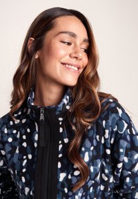 Blue and black fleece jacket features a zippered front and a high collar, adorned with an abstract pattern in white and light blue.