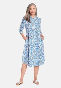 Hellblau gemustertes Hemdkleid mit knopflosem Vorderteil, Dreiviertelärmel, Taschen und einem schwingenden Rock. Der Stoff wirkt leicht und atmungsaktiv.
