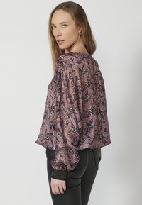 Langärmlige, lila Paisley-Bluse mit Rüschenärmeln und schwarzen strukturierten Bündchen. Leichtes, fließendes Material mit einer drapierten Silhouette.