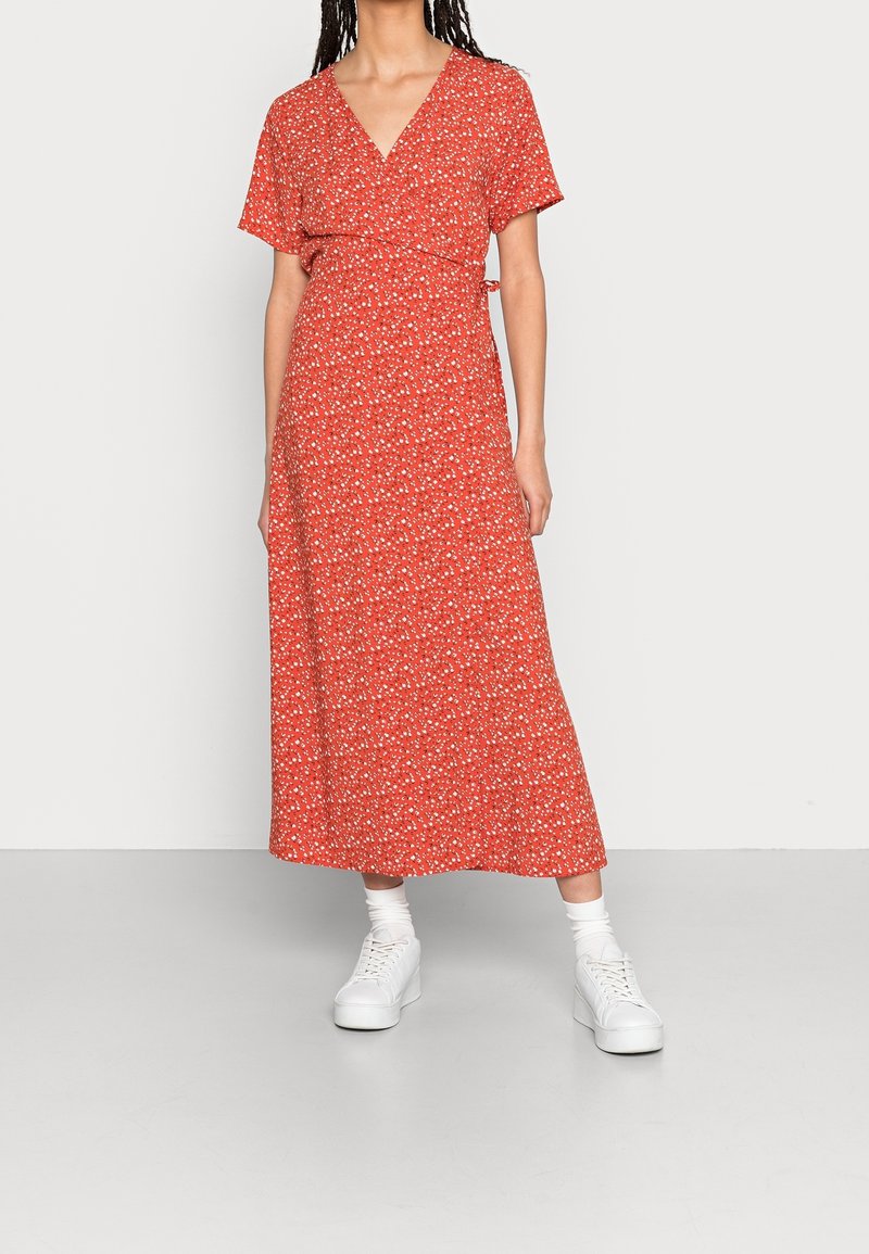 Femme portant une robe portefeuille rouge à fleurs avec des manches courtes, associée à des chaussettes blanches et des baskets compensées blanches.