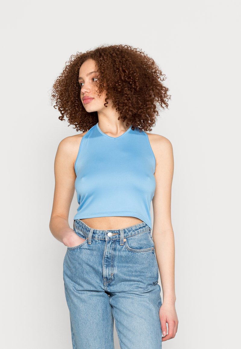 Top cropped azul claro feito de tecido suave, com decote redondo e design sem mangas, estilizado com jeans de cintura alta.