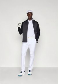 Golfo apranga, kurioje yra juoda striukė, balta polo marškinėliai, balti kelnės ir balti batai su mėlynais akcentais. Aksesuarai – balta kepurė ir pirštinė.