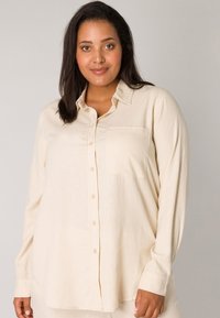 Light beige long-sleeve button-up shirt with a single chest pocket, made of soft fabric, featuring a relaxed fit and classic collar design.