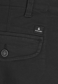 Gros plan d'une poche en tissu noir avec un bouton et une étiquette de la marque Jack & Jones cousue près du bord supérieur.
