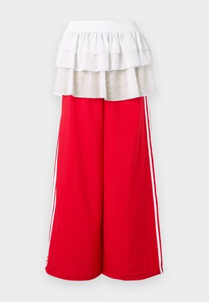 Piros, széles szárú nadrág fehér oldalsávokkal, fehér, réteges fodros felülrésszel. Rugalmas derékrész a kényelemért. Puha anyag textúra.