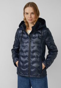 Doudoune bleu marine avec capuche, présentant un design matelassé, une fermeture éclair et des poches latérales. Fabriquée en matériau léger et brillant.
