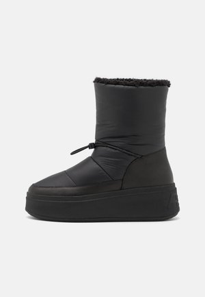 Bota de invierno aislada negra con suela plataforma gruesa, cordón ajustable alrededor del tobillo y forro de lana en el borde superior.