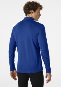Dlouhý rukáv, modré sportovní tričko vyrobené z texturované látky, s límečkem a kontrastním šitím podél rukávů a boků.