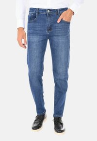 Jeans in denim blu con una vestibilità dritta, design a cinque tasche e cuciture a contrasto. Indossati con scarpe nere e una camicia bianca a maniche lunghe.