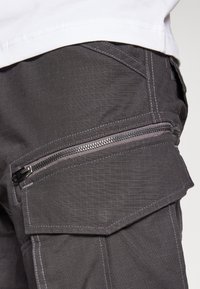 Šedé cargo kalhoty s mřížkovou texturou, vybavené boční kapsou na zip a kontrastním prošíváním. Odolná tkanina s praktickými designovými prvky.