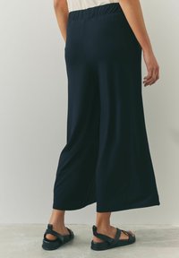 Pantalones de pierna ancha de color navy con cintura elástica, hechos de una tela suave. Combinados con sandalias negras de tiras anchas y suela gruesa.