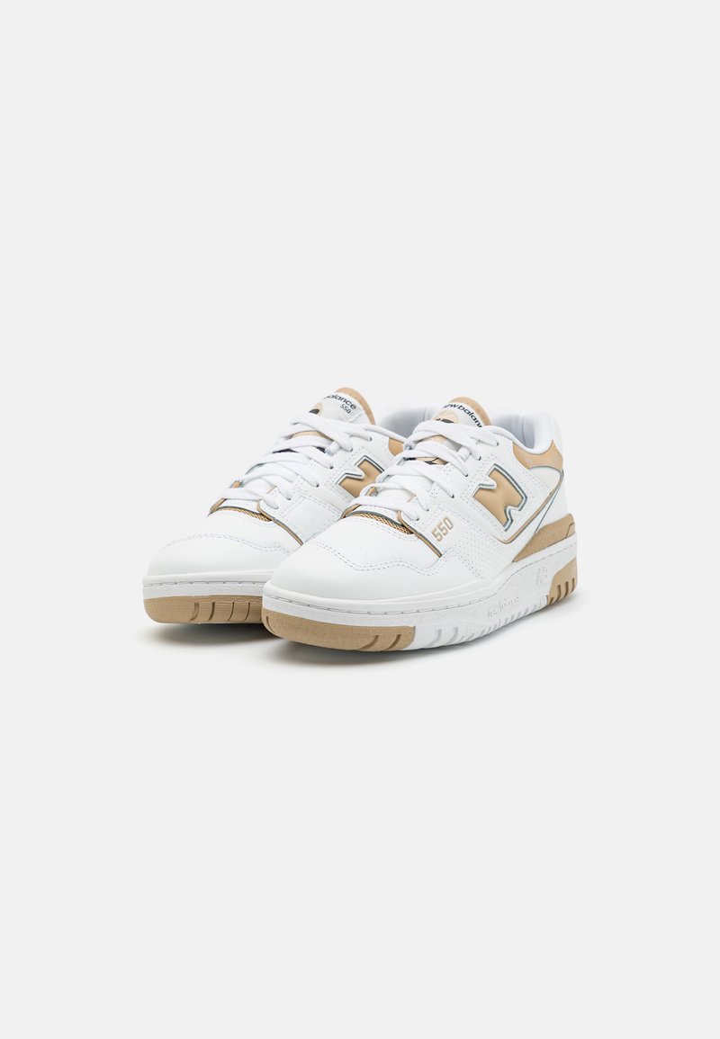 Chaussures de sport blanches avec des accents beige, dotées d'un système de laçage, en cuir texturé et d'une semelle en caoutchouc avec des rainures horizontales. Numéro de modèle 550.