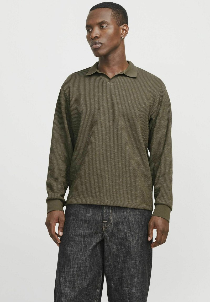 Polo de manga larga en verde oliva con textura acanalada, cuello y puños. Combinado con pantalones de mezclilla oscuros. Diseño simple y funcional.