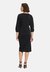 Musta mekko, jossa on kimalteleva tekstuuri, 3/4-puffihihat, vartalonmyötäinen siluetti, polven pituinen helma, yhdistettynä remmirakkaitten korkokenkien kanssa.