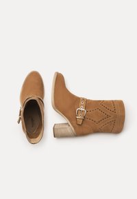Hellbraune Wildleder-Stiefeletten mit einer spitzen Kappe, einem Holz-Blockabsatz, dekorativen Durchbruchmustern und einem Schnallenriemen.