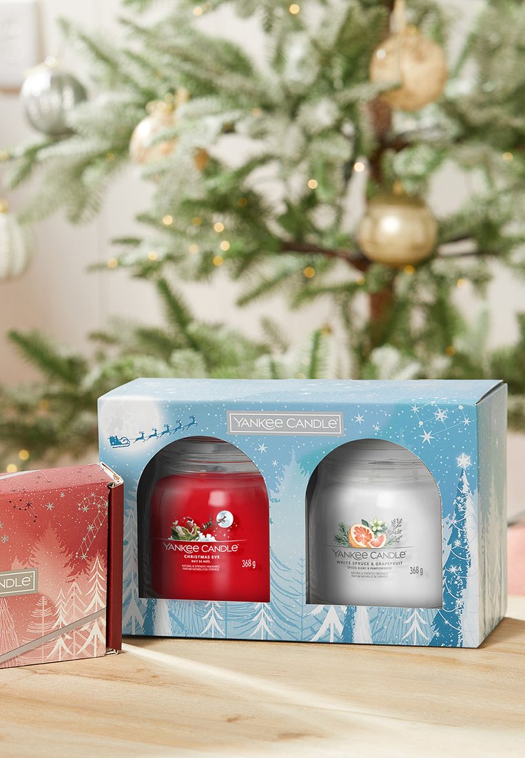 Vasetti Yankee Candle rossi e bianchi in una scatola blu con design invernale; contiene le fragranze "Natale Vigilia" e "Spezie Bianche e Pompelmo."