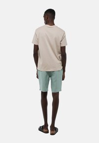 T-shirt en coton beige, shorts vert clair et sandales noires. Modèle vu de dos, avec un design simple et décontracté.