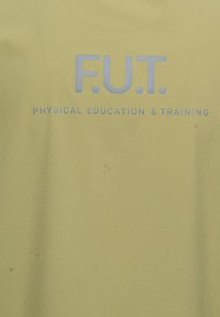 Żółta tkanina z szarym tekstem "F.U.T." nad mniejszym tekstem "WYCHOWANIE FIZYCZNE I TRENING" wyśrodkowanym na powierzchni.