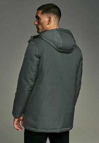 Chaqueta gris aislante con capucha, que presenta una textura suave, mangas largas y un dobladillo recto. Diseñada para brindar calor y protección.