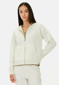 Lichtcreme rits-hoodie in een textuur breisel, met een voorzak en geribbelde boorden, gecombineerd met een beige top.