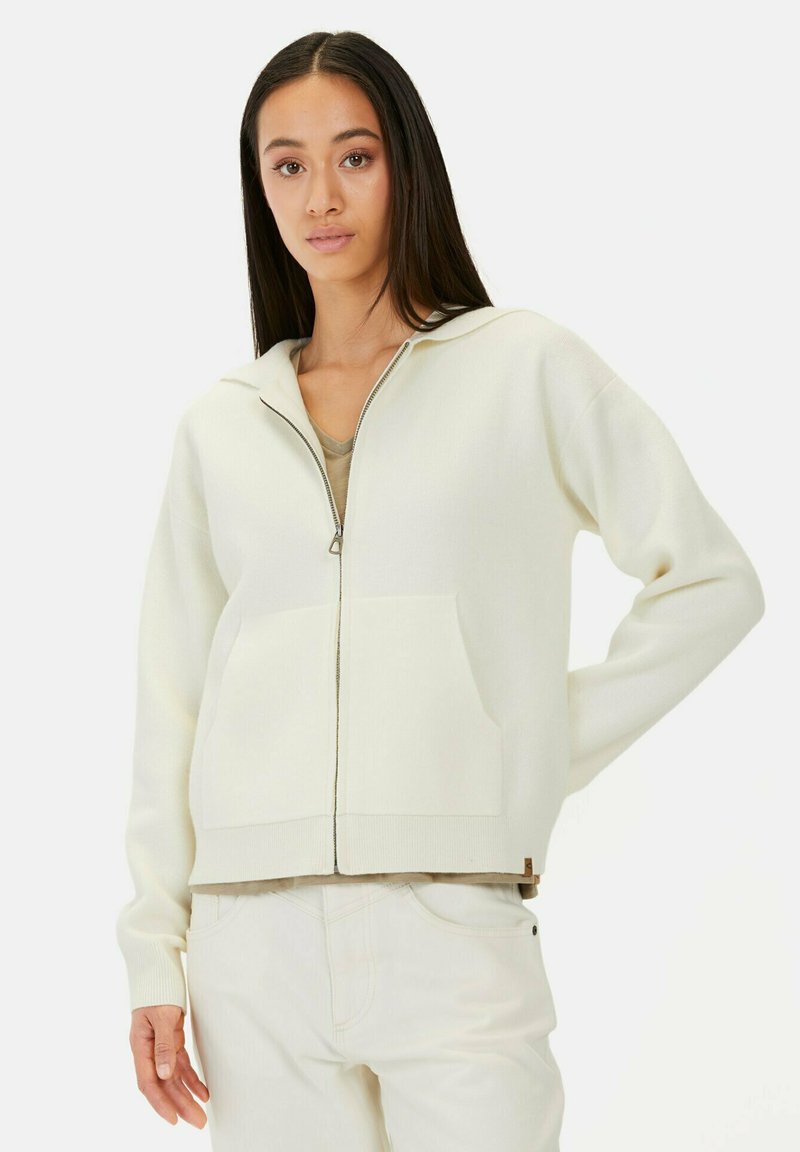 Lyscremet zip-hoodie i struktureret strik, med en frontlomme og ribbede ærmer, parret med en beige top.