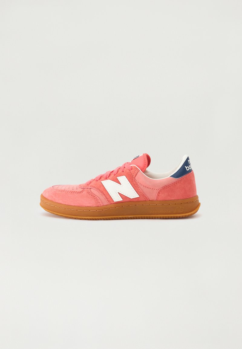 Różowe zamszowe sneakersy z białym logo "N", białą językiem, gumową podeszwą i granatowym akcentem na pięcie. Posiadają perforowane detale i płaskie sznurowadła.