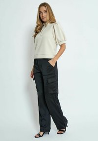 Beige cropped sweatshirt with a zip neck, puff sleeves, paired with black cargo pants featuring side pockets, and black heeled sandals.