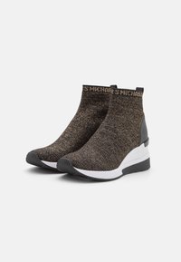 Bottines tricotées noires et dorées avec un talon compensé, dotées d'une semelle blanche et d'un logo en relief sur le bord supérieur. Surface texturée.