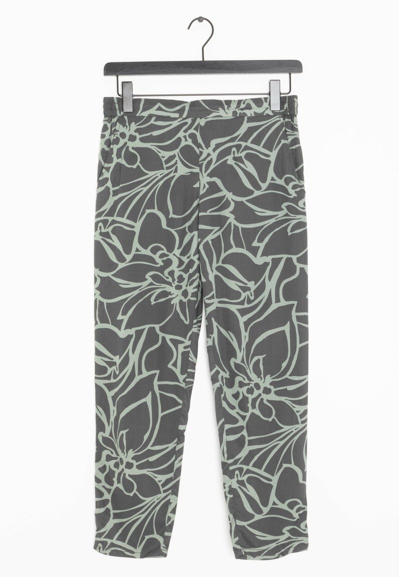 Pantalon gris foncé avec motif floral abstrait vert clair accroché sur un cintre noir en bois contre un fond blanc.