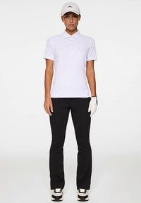 Witte korte mouw polo met een gestructureerd design, gecombineerd met zwarte broek. Een witte pet en witte golfhandschoen maken de look compleet.