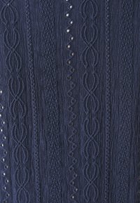 Tessuto texturizzato blu navy con motivi intricati che presentano sezioni in rilievo e piatte, insieme a piccoli dettagli intagliati che creano un interesse visivo.
