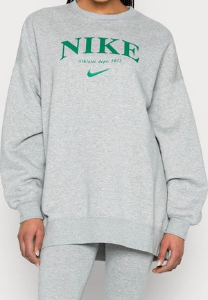 Personne portant un sweat-shirt oversize gris clair et un legging avec le logo vert « NIKE Athletic dept. 1972 » et le swoosh sur la poitrine.