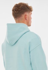 Felpa leggera blu con un grande cappuccio, caratterizzata da un colore uniforme. Il tessuto sembra morbido, con una vestibilità relax e cuciture sulle spalle abbassate.